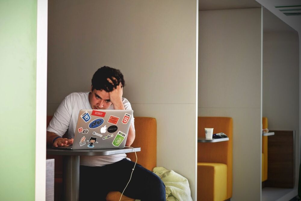 Een jongen met zijn hand in zijn haren achter de laptop